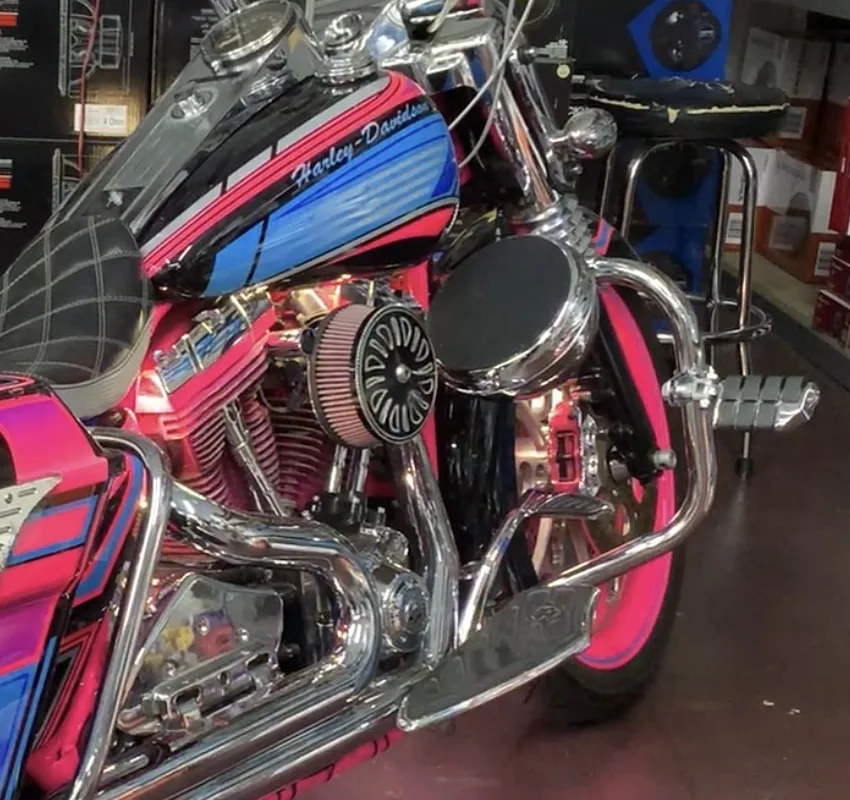 Chrome AMS Pod on the engine guard of a pink and blue Harley-Davidson Road King in the Carson showroom